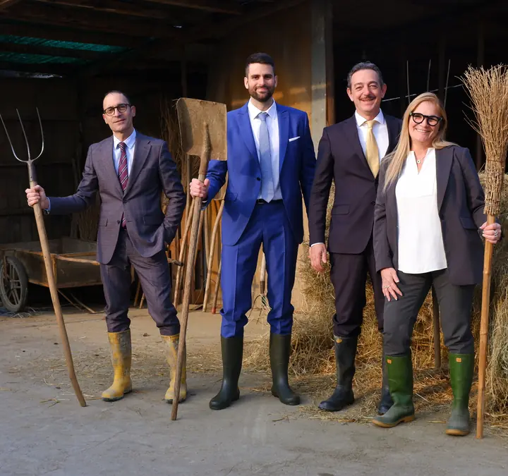 I quattro soci di Fattoria dei Talenti nel fienile, in giacca e stivali di gomma, con forconi e pala